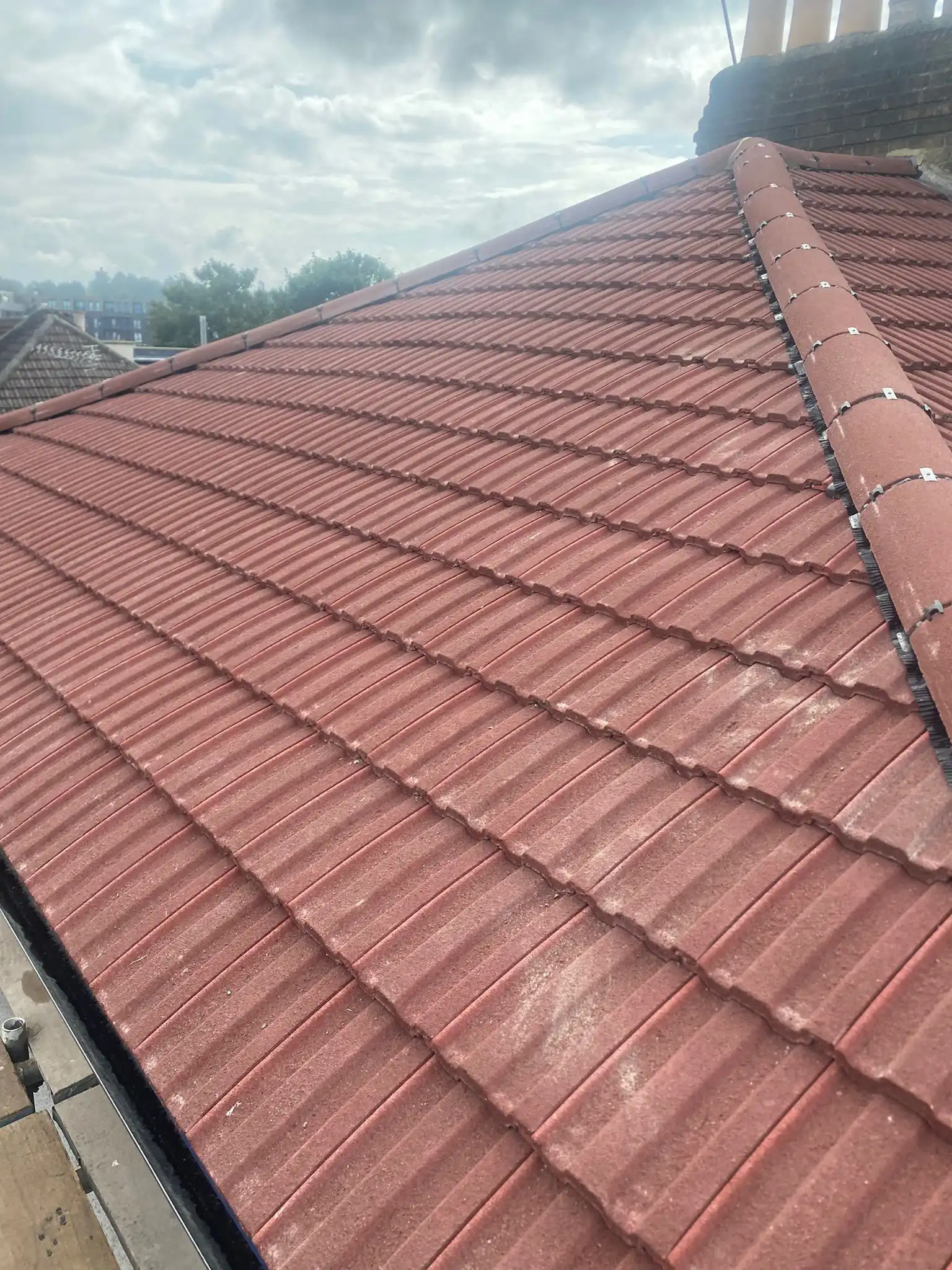 A close-up view of a red tiled roof under a cloudy sky, showing the texture and layout of the tiles.